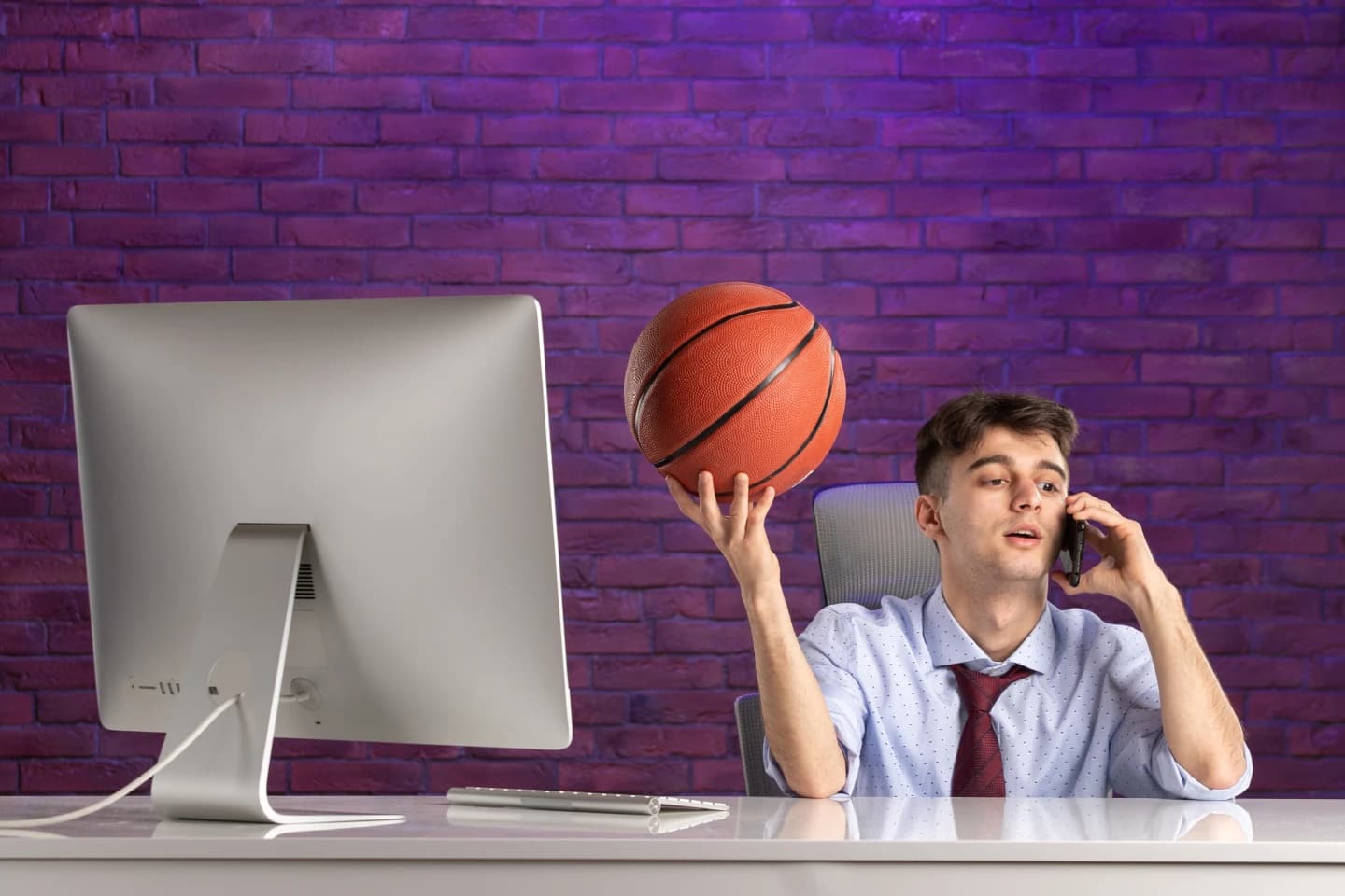 Front view office worker behind office desk holding basketball and talking at phone